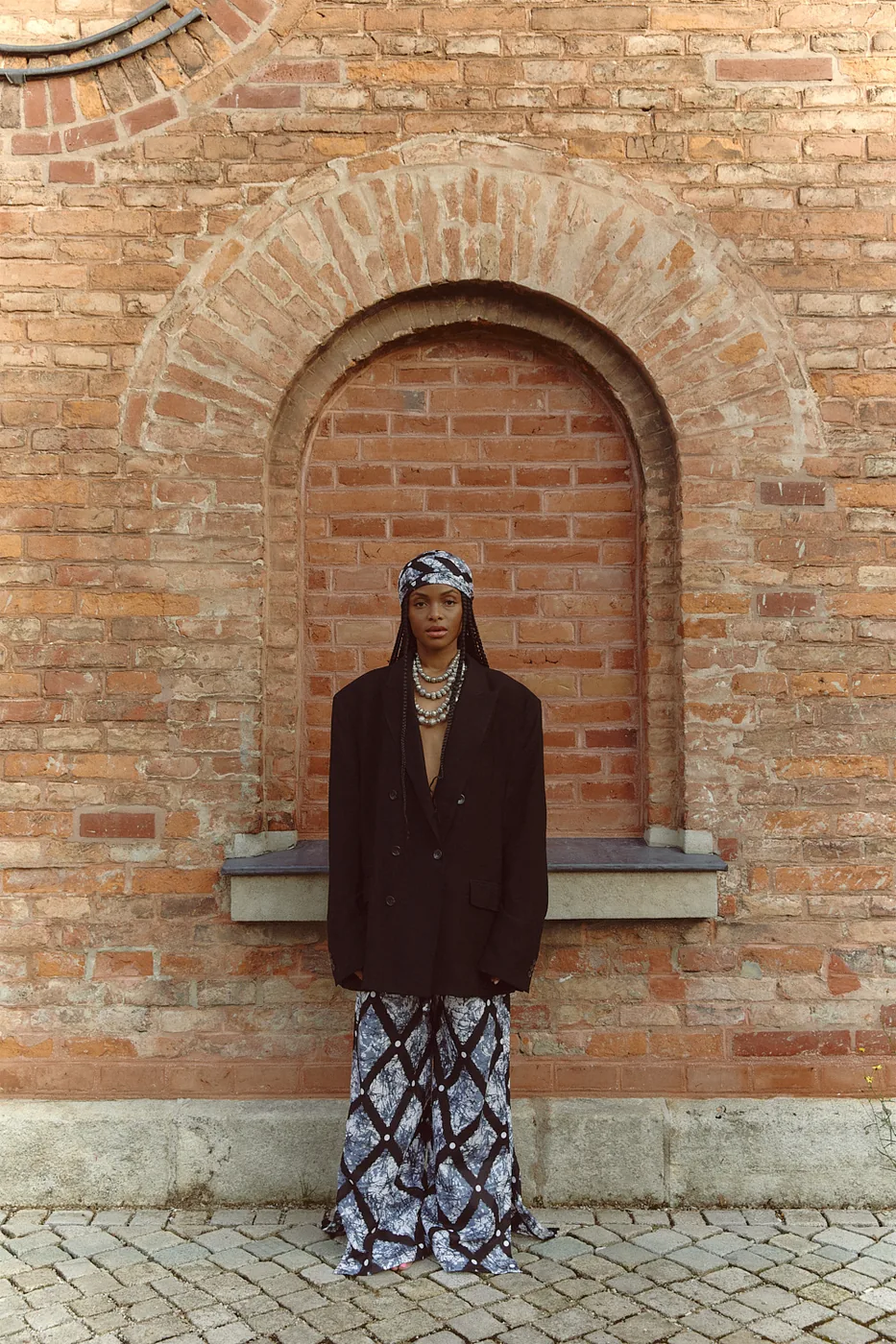 Model in a printed skirt and dark blazer framed by a brick archway.