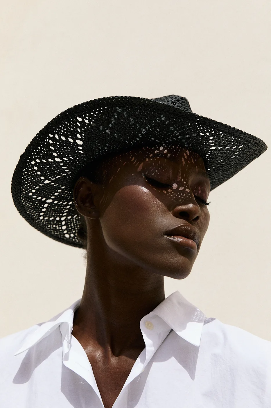 Portrait of a model in a wide black woven hat and crisp white shirt.